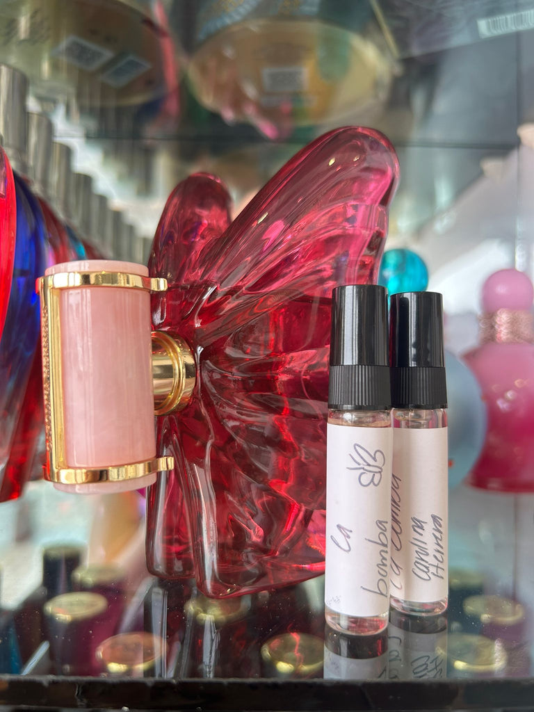 Two small perfume bottles with black caps and white labels in front of a large decorative butterfly.